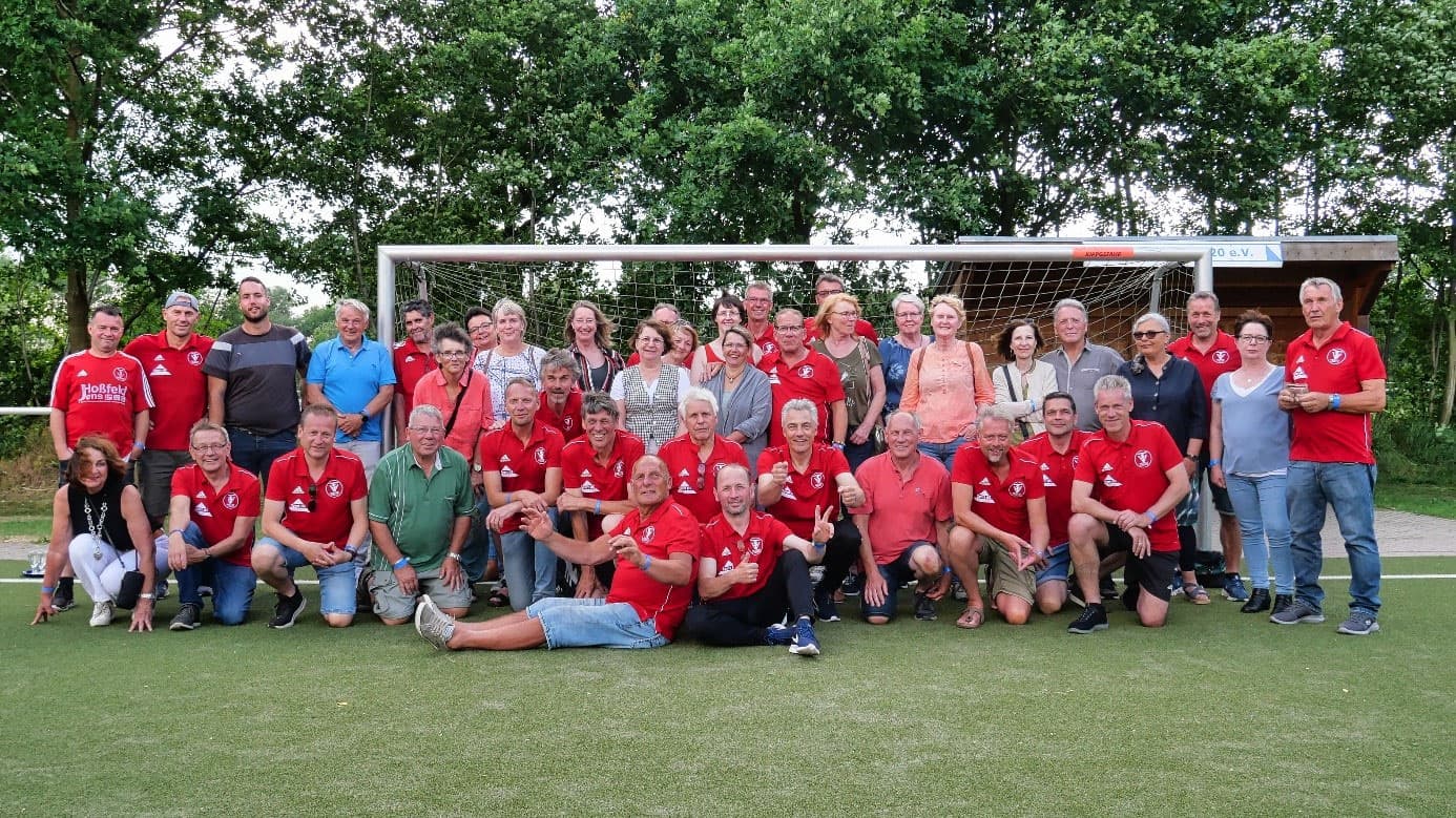 Gruppenfoto in roten Vereinstrikots mit Begleitung vor einem Fußballtor